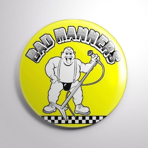 May include: A yellow button with a black and white illustration of a cartoon character holding a microphone. The text "BAD MANNERS" is written in a black, stylized font around the character.