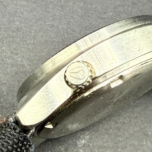 May include: A silver wristwatch with a black fabric band. The watch has a round face and a silver bezel with a small crown on the right side.