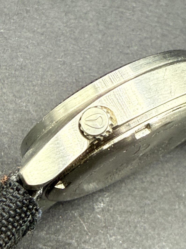 May include: A silver wristwatch with a black fabric band. The watch has a round face and a silver bezel with a small crown on the right side.
