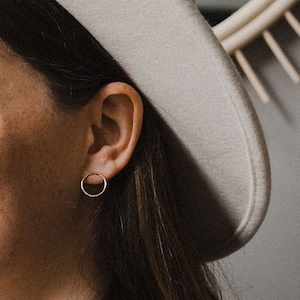 May include: A woman wearing a white fedora hat with a small gold hoop earring in her right ear.