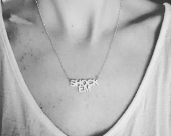 May include: A silver necklace with a pendant that reads "SHOCK EM".