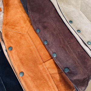 Puede incluir: Primer plano de varios chalecos de ante en tonos naranja, marr&oacute;n y beige. Cada chaleco presenta una parte delantera abotonada y un dise&ntilde;o a medida. Los chalecos se muestran con sus forros interiores visibles.