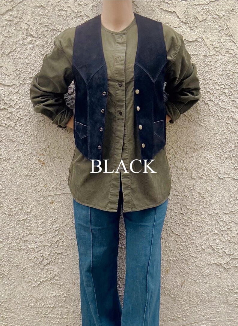 Puede incluir: Un chaleco de ante negro con botones plateados se usa sobre una camisa verde abotonada y unos vaqueros azules. La palabra "BLACK" se muestra en letras blancas en el centro de la imagen. El atuendo es informal y vintage.