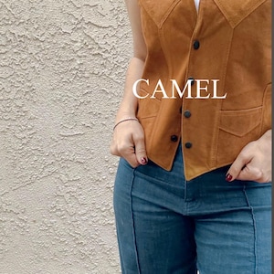Puede incluir: Chaleco de ante color camel con dise&ntilde;o de cuello en V y botones negros. El chaleco tiene dos bolsillos delanteros y se lleva sobre una camiseta blanca. La palabra "CAMEL" est&aacute; impresa en el chaleco. El modelo lleva vaqueros azules.