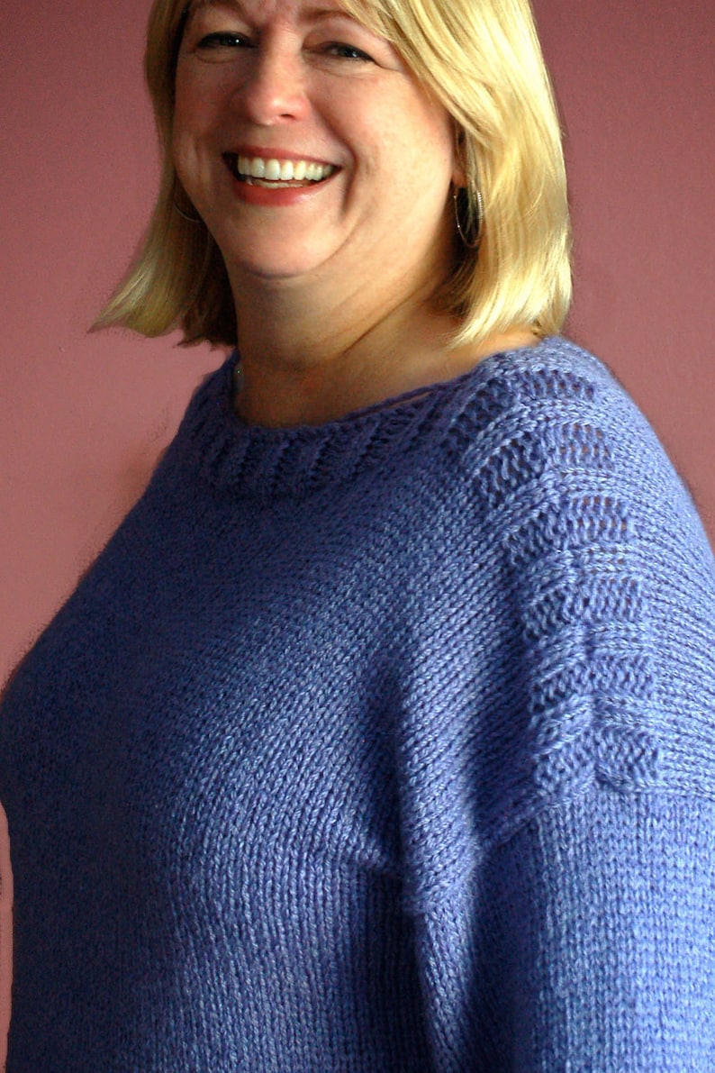 May include: A woman wearing a purple knitted sweater with a delicate lace pattern around the neckline and shoulders.