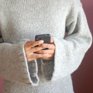 May include: A gray knitted sweater with long sleeves and a wide, boat neck. The sweater is made of a soft, fuzzy yarn and has a relaxed fit.