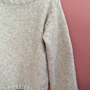 May include: A light gray knitted sweater with a boat neck and long sleeves.
