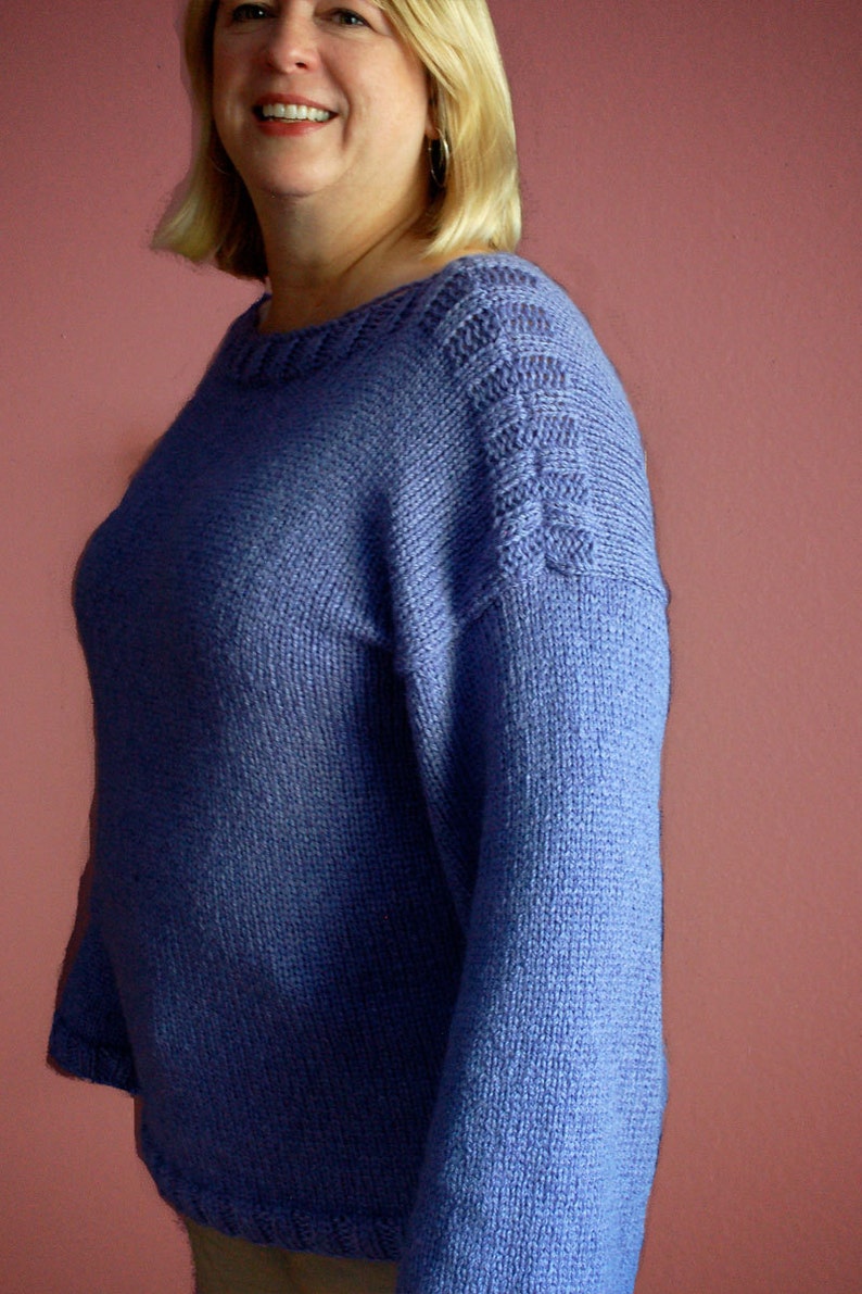 May include: A woman wearing a purple knitted sweater with a cable knit design on the shoulder.