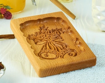 May include: A wooden cookie cutter with a floral design, a brown cookie with the same design, and other baking ingredients, including honey, cinnamon sticks, star anise, and eggs.