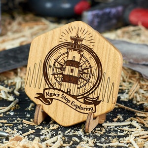 Könnte beinhalten: Ein sechseckiges Holzschild mit einem Leuchtturm- und Kompassdesign. Das Schild ist mit dem Text "Never Stop Exploring" graviert. Das Schild steht auf einem kleinen Holzständer und ist von Holzspänen umgeben.
