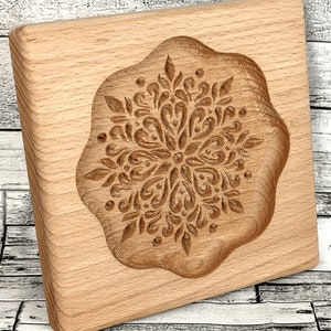 May include: A wooden cookie cutter with a detailed snowflake design. The cutter is made of light brown wood and has a smooth, rounded edge.