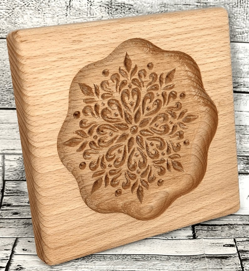 May include: A wooden cookie cutter with a detailed snowflake design. The cutter is made of light brown wood and has a smooth, rounded edge.
