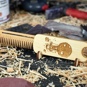 Puede incluir: Un peine de madera con un soporte, que presenta un diseño grabado con láser de un astronauta en la luna. El peine está hecho de madera marrón claro y tiene un acabado natural.