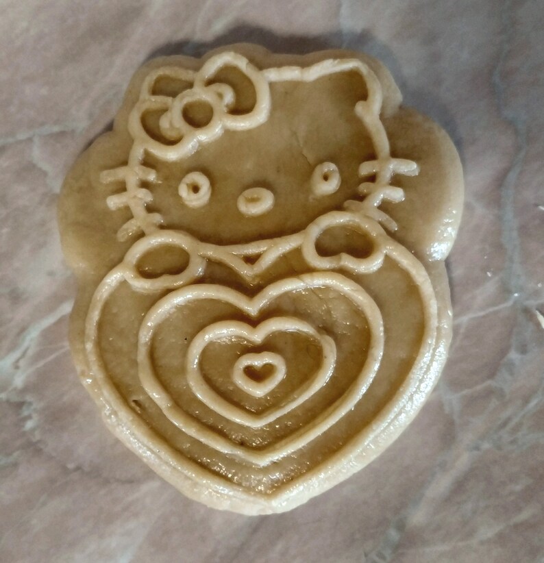 Puede incluir: Una galleta marr&oacute;n con un dise&ntilde;o de Hello Kitty. La galleta tiene forma de coraz&oacute;n con tres c&iacute;rculos conc&eacute;ntricos en su interior.
