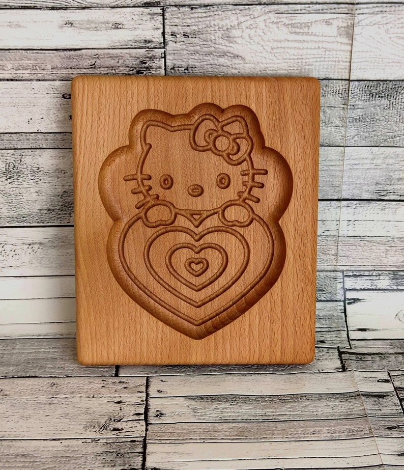 Puede incluir: Un cortador de galletas de madera con forma de Hello Kitty sosteniendo un coraz&oacute;n. El cortador tiene un dise&ntilde;o detallado con m&uacute;ltiples formas de coraz&oacute;n.