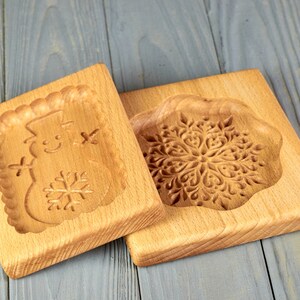 May include: Two wooden cookie cutters, one with a snowflake design and the other with a snowman design. The cutters are made of light brown wood and have a smooth finish.