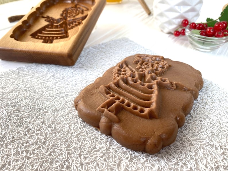 May include: A brown gingerbread cookie with an embossed design of an angel. The cookie is sitting on a white lace doily.