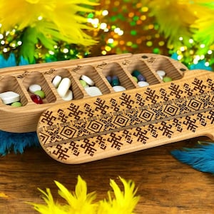May include: Wooden pill box with seven compartments labeled Sun, Mon, Tue, Wed, Thu, Fri, and Sat. The box is decorated with a geometric pattern and has a lid that opens to reveal the compartments.