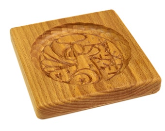 May include: A wooden cookie cutter with a carved design of a Christmas angel with stars and a crescent moon. The cutter is made of light brown wood and has a square shape.
