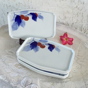 May include: Set of four white ceramic plates with a blue and red floral design. The plates are slightly curved and have a rounded edge.