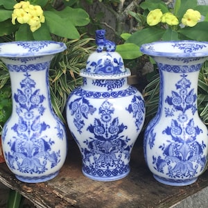 May include: Three blue and white porcelain vases with intricate floral designs. The centre vase has a lid with a small blue and white animal figurine on top.