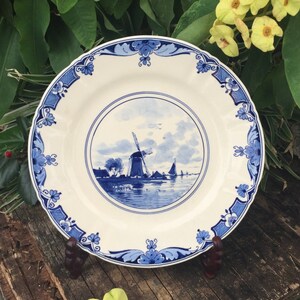 May include: A blue and white porcelain plate featuring a Dutch windmill scene. The plate has a scalloped edge and a floral design.