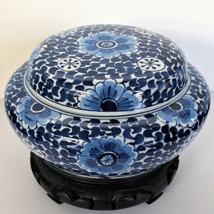 Puede incluir: Un jarrón de porcelana azul y blanco con un diseño floral. El jarrón está sobre un soporte de madera.