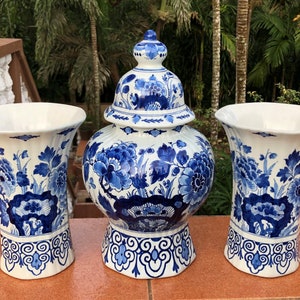 May include: A set of three ceramic vases and a lidded jar with a blue and white floral design. The vases have a flared shape, and the jar has a rounded body. The set is placed on a brown surface, with a natural background.