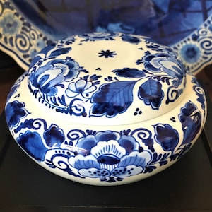 Puede incluir: Un tarro de cerámica blanca con un diseño floral azul y blanco. El tarro tiene una tapa y está decorado con motivos tradicionales holandeses de Delft.
