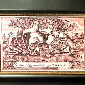 May include: A framed tile depicting a scene of people interacting with a cow. The tile is decorated with a pink and white floral pattern and the text "Die pleit om een koe geeft er een toe".