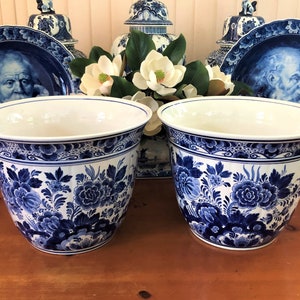 Op de afbeelding: Twee blauwe en witte Delftse potten met bloemenmotieven. De potten zijn rond en hebben een brede basis.