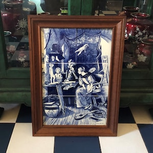 May include: A framed artwork featuring a blue and white illustration. The artwork depicts a scene with figures in a room, with a flying figure. The frame is made of brown wood. The artwork is displayed on a checkered floor.