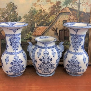 May include: Three blue and white Delftware vases with floral designs. The vases are on a wooden surface.