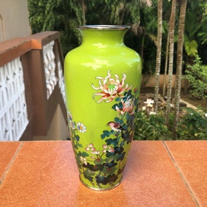 May include: A bright green vase with a silver rim and base. The vase features a floral and bird design in pink, white, and blue. The vase is a decorative item.