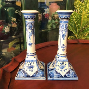May include: Pair of blue and white ceramic candlestick holders with intricate floral designs. The candlesticks have a square base and a tall, slender column.