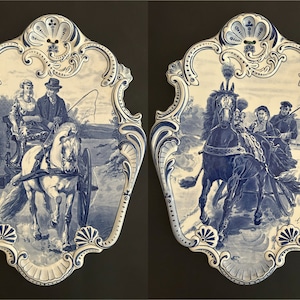 Op de afbeelding: Twee bijpassende, blauw-witte decoratieve keramische wandplaten. Elke plaat toont een gedetailleerde illustratie van een paardenkoets met mensen. De platen hebben een sierlijke, geschulpte rand.