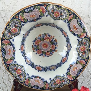 K&ouml;nnte beinhalten: Eine gro&szlig;e, wei&szlig;e Keramiksch&uuml;ssel mit einem gewellten Rand. Die Sch&uuml;ssel ist mit einem blauen, gr&uuml;nen und rosa Blumenmuster verziert. Die Sch&uuml;ssel ist perfekt zum Servieren von Salaten, Obst oder anderen Gerichten.