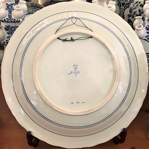 May include: A white ceramic plate with blue and white floral designs. The back of the plate has a blue and white stamp that reads "Delft" and "ww. 187. an."