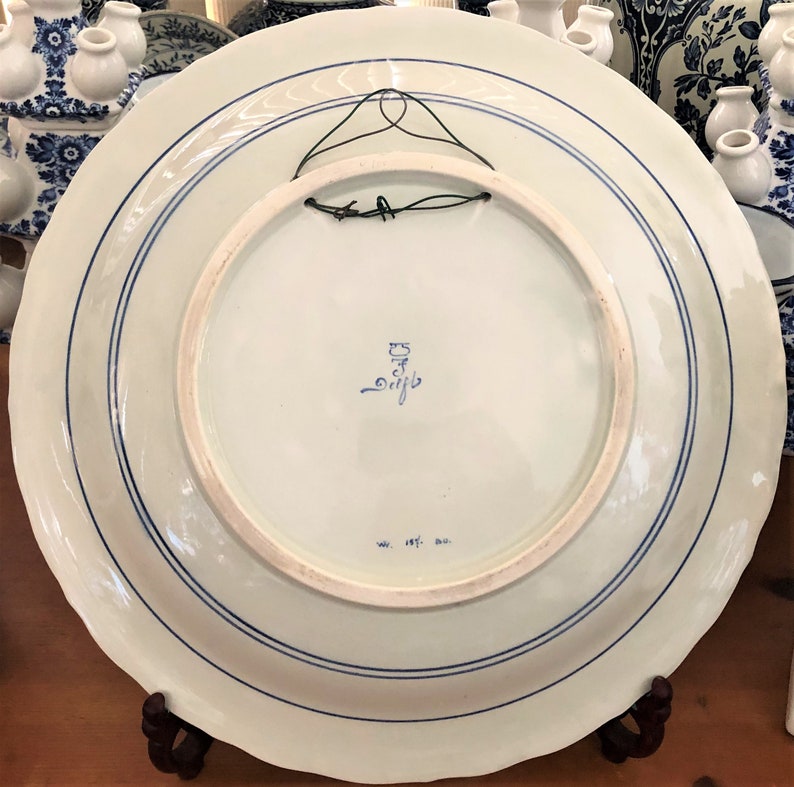 May include: A white ceramic plate with blue and white floral designs. The back of the plate has a blue and white stamp that reads "Delft" and "ww. 187. an."