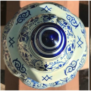 May include: A three-part image of a blue and white ceramic jar with a lid. The jar has a scalloped edge and is decorated with floral and scroll patterns. The lid has a knob and is also decorated with blue and white designs. The bottom of the jar is light blue.