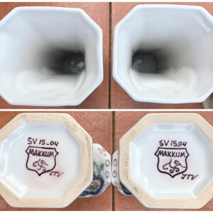 Puede incluir: Dos jarrones de cer&aacute;mica blanca con un patr&oacute;n floral azul y blanco. La parte inferior de cada jarr&oacute;n tiene un sello marr&oacute;n que dice "SV 15-04 MAKKUM" con un dise&ntilde;o estilizado y las letras "JTV".