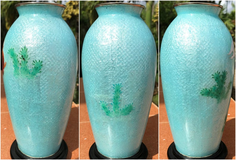 Pu&ograve; includere: Un vaso in ceramica blu chiaro con una superficie testurizzata e disegni floreali verdi. Il vaso &egrave; su un piedistallo nero.