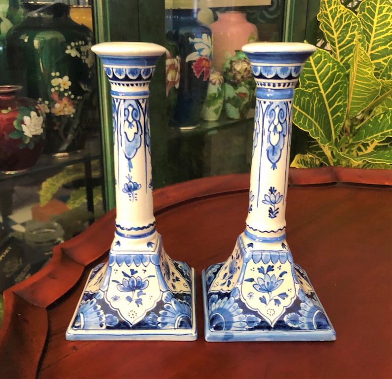 May include: Pair of blue and white ceramic candlestick holders with intricate floral designs. The candlesticks have a square base and a tall, slender column.