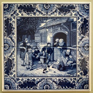 May include: A blue and white Delft tile depicting a scene of people gathered outside a building. The tile has a decorative border of blue and white flowers. The text "De Witte Bloem" and "Maasdriessen van Ostade" are visible on the tile.