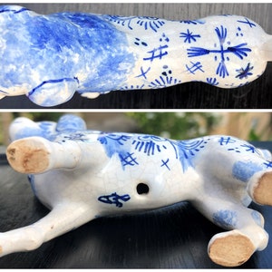 Puede incluir: Figura de cer&aacute;mica blanca y azul de un animal reclinado. El dise&ntilde;o azul presenta patrones florales y geom&eacute;tricos. La parte inferior muestra las patas, un peque&ntilde;o agujero y una marca del fabricante.