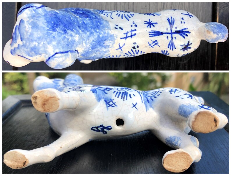 Puede incluir: Figura de cer&aacute;mica blanca y azul de un animal reclinado. El dise&ntilde;o azul presenta patrones florales y geom&eacute;tricos. La parte inferior muestra las patas, un peque&ntilde;o agujero y una marca del fabricante.