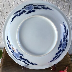 Op de afbeelding: Een witte keramische plaat met een blauw bloemen- en wolkenontwerp rond de rand. De plaat heeft een licht verhoogde rand en een gladde, glanzende afwerking. Het ontwerp is een traditioneel Aziatisch ge&iuml;nspireerd patroon.