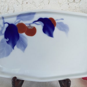 May include: A white rectangular ceramic serving tray with a blue and red floral design. The design features a branch with blue leaves and red fruit.