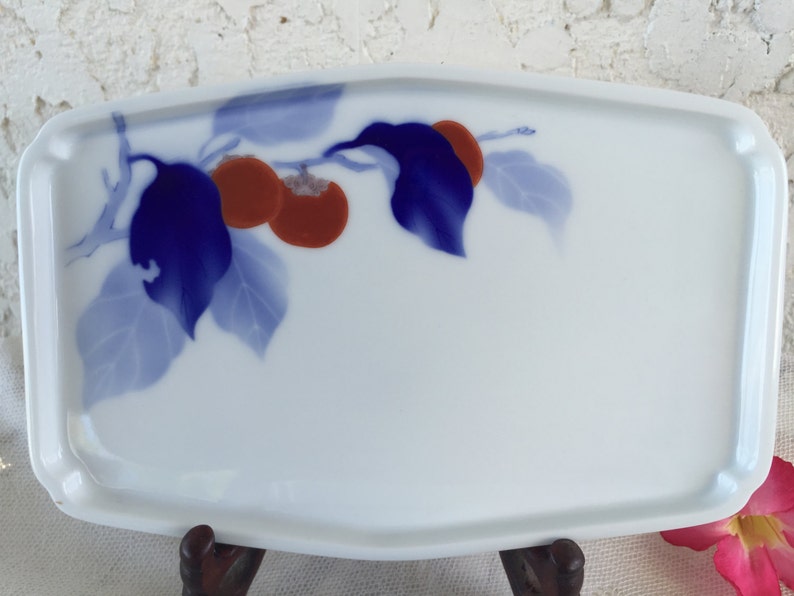 May include: A white rectangular ceramic serving tray with a blue and red floral design. The design features a branch with blue leaves and red fruit.
