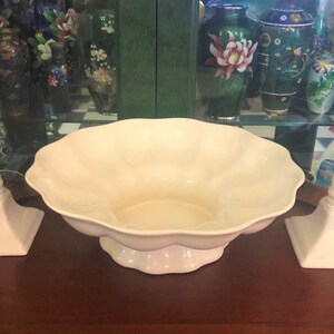 May include: Two white ceramic candle holders with square bases and a white ceramic bowl with a scalloped edge.